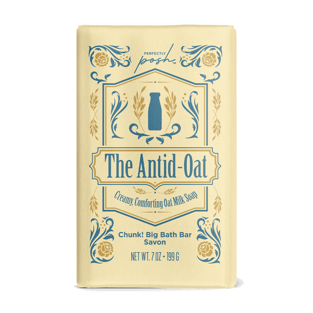 A yellow The Antid-Oat Chunk Big Bath Bar by Perfectly Posh features blue and gold floral designs, a milk bottle graphic, and “Creamy, Comforting Oat Milk Soap” text. Gently exfoliates and soothes dry, sensitive skin. Net Wt. 7 oz (199 g).