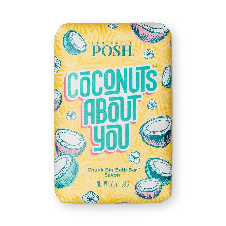 The Perfectly Posh Coconuts About You Chunk Big Bath Bar is a moisturizing, sulfate-free coconut bath bar in yellow and aqua packaging with coconut and floral designs. The wrapper displays the product and brand name.